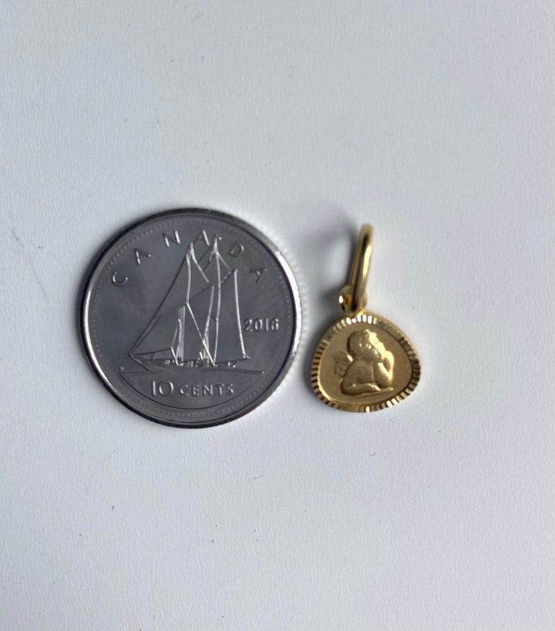May include: A gold-colored angel charm pendant with a detailed design. The charm is about the size of a Canadian 10-cent coin.