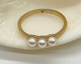 May include: A gold ring with three small white pearls set in a row.