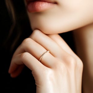 May include: A close-up of a hand wearing a thin, gold, twisted band ring.