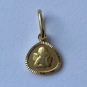 May include: A gold charm featuring a detailed depiction of a cherub angel with wings, resting its head on its hand. The charm is in the shape of a teardrop with a decorative border.