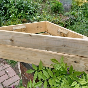 May include: A triangular wooden planter made from reclaimed wood planks. The planter is empty and ready for planting.