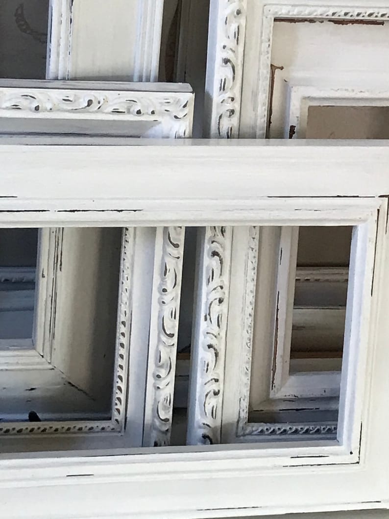 May include: A collection of white, ornate picture frames with distressed edges. The frames vary in size and design, some featuring detailed carvings and others with simpler, clean lines. The overall aesthetic is vintage and shabby chic.