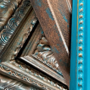 May include: Close-up of several decorative picture frames. The frames have ornate detailing and are painted in shades of brown, teal, and turquoise. The frames are stacked together, showcasing their different textures and colors.