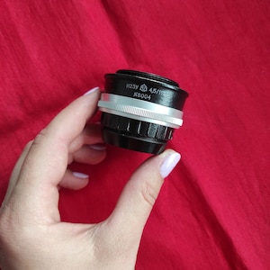 Op de afbeelding: Een zwarte camera lens met zilveren accenten. De lens heeft de tekst "W23Y 4,5/110 N8004" erop gedrukt.