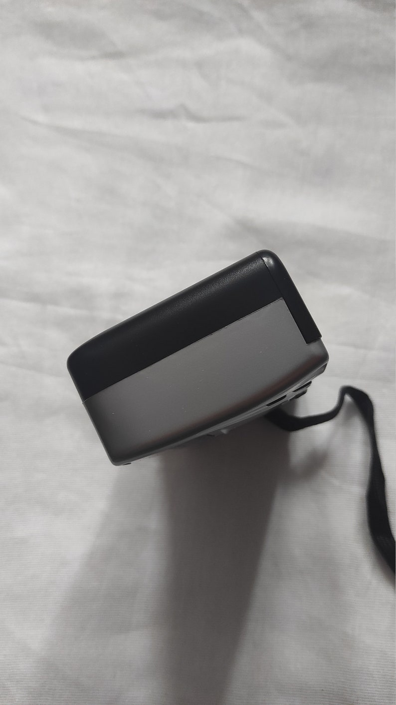 Puede incluir: Un dispositivo electr&oacute;nico negro y gris con una correa negra. El dispositivo tiene una forma rectangular y una superficie lisa.