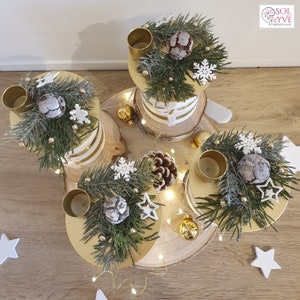 May include: A gold and white tiered candle holder with four candle holders, decorated with pine branches, pinecones, snowflakes, and gold stars. The candle holder is on a wooden base with white lights.