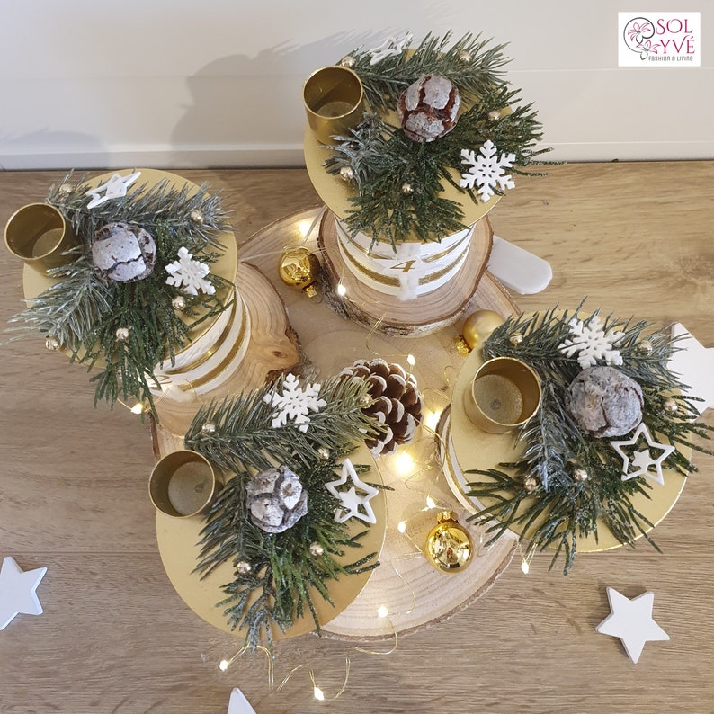 May include: A gold and white tiered candle holder with four candle holders, decorated with pine branches, pinecones, snowflakes, and gold stars. The candle holder is on a wooden base with white lights.