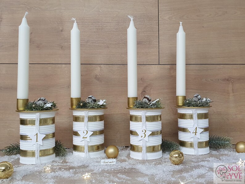 May include: Four white candlesticks with gold accents and numbers 1 through 4 on each. Each candlestick is decorated with a small sprig of greenery and gold ribbon.