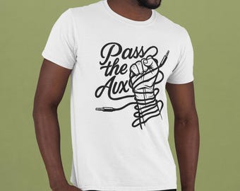Può includere: T-shirt bianca con un design grafico nero. Il design presenta un pugno chiuso avvolto in un cavo audio, con le parole "Pass the Aux" in un font stilizzato. La maglietta è a girocollo e maniche corte.