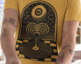 Può includere: T-shirt giallo senape con grafica nera. Il design include un occhio, stelle e un vortice a forma di cuore su un motivo a scacchi. La maglietta a maniche corte è realizzata in materiale morbido.