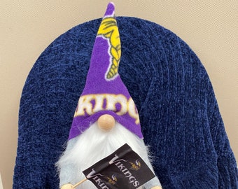 May include: A purple and yellow gnome wearing a hat and pants with the word "Vikings" on them. The gnome is holding a small flag that also says "Vikings".