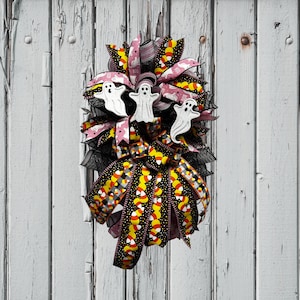 May include: A Halloween wreath with a pink and black ribbon bow, featuring candy corn and ghost designs. The wreath is decorated with white ghosts with the word "Boo" on them.