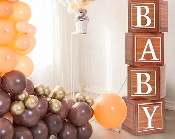 May include: Wooden blocks spelling out the word "BABY" in white letters. The blocks are stacked on top of each other and have a wood grain pattern. The blocks are surrounded by brown and orange balloons.