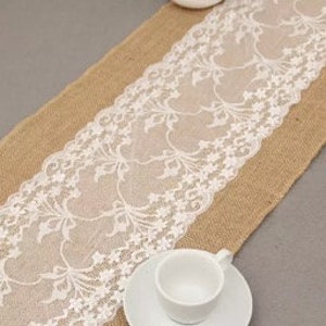 May include: A burlap table runner with a white lace trim. The lace has a floral design.