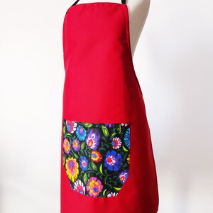 K&ouml;nnte beinhalten: Rote Sch&uuml;rze mit einer gro&szlig;en Tasche mit Blumendruck. Die Sch&uuml;rze hat schwarze Tr&auml;ger.