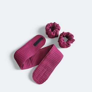 Op de afbeelding: Een set van drie bordeauxrode haaraccessoires. De set bevat een hoofdband met een klittenbandsluiting en twee scrunchies.