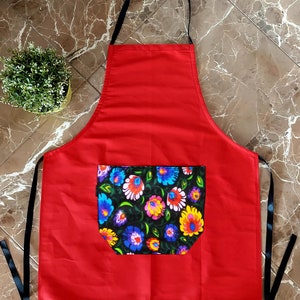 K&ouml;nnte beinhalten: Rote K&uuml;chensch&uuml;rze mit einer schwarzen Tasche mit Blumendruck. Die Sch&uuml;rze hat verstellbare schwarze Tr&auml;ger.