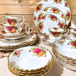 Peut inclure: Service à thé en porcelaine blanche orné de motifs floraux de roses rouges, roses et jaunes. L'ensemble comprend des assiettes, des tasses, des soucoupes et des bols avec des bordures dorées. Fond en bois brun clair.