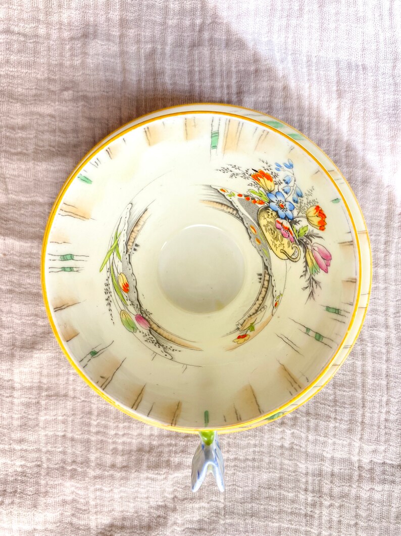 May include: A vintage teacup with a floral design in shades of pink, blue, yellow, and green. The cup has a yellow rim and a delicate floral pattern on the inside.