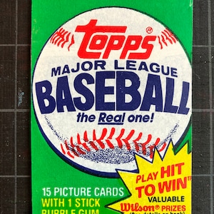 May include: A vintage Topps Major League Baseball trading card pack featuring a baseball graphic with red stitching and the text "Play Hit To Win" with a yellow starburst. The pack includes 15 picture cards and one stick of bubble gum.  Valuable Wilson prizes are included. See details on the back.