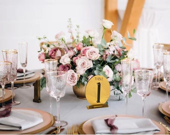 May include: Gold table number card with the text "Table 1" on a white table with pink flowers and glasses.