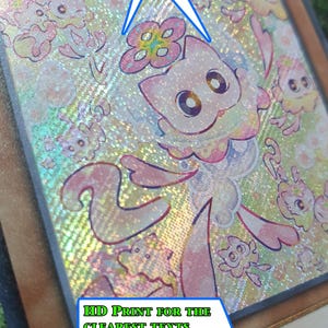 May include: A holographic trading card titled Lil Charmy Meowls featuring a central cat character with pink and white fur, surrounded by smaller cat figures, with text overlays stating Different levels of transparency like the real ones and HD print for the clearest texts.