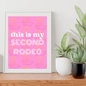 Puede incluir: Arte de pared imprimible rosa con fondo blanco y el texto "this is my SECOND RODEO" en blanco. El fondo está lleno de un patrón de botas de vaquero naranjas.