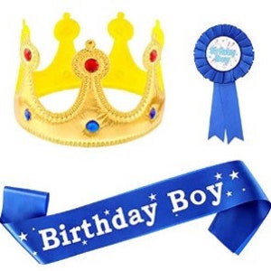 Puede incluir: Un conjunto de fiesta de cumplea&ntilde;os azul y dorado con una corona, una banda y una cinta azul con una estrella blanca y las palabras "Feliz cumplea&ntilde;os" en ella.