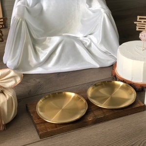 May include: Two gold metal serving trays on a wooden tray. The trays are round and have a shiny finish. The wooden tray is brown and has a rustic look.