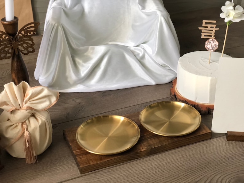 May include: Two gold metal serving trays on a wooden tray. The trays are round and have a shiny finish. The wooden tray is brown and has a rustic look.