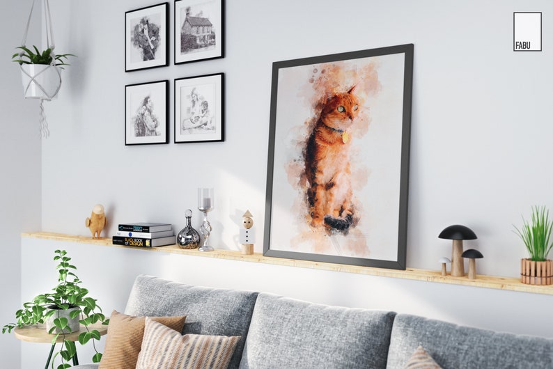 May include: A watercolor painting of a ginger cat with green eyes, sitting on a white background. The painting is framed in a black frame and hanging on a white wall. The cat is wearing a collar with a tag.