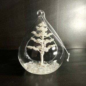 May include: A clear glass bauble containing a silver wire tree. The tree is surrounded by white glitter.