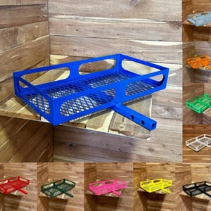 May include: A blue metal cargo carrier with a mesh bottom and a hitch receiver. The carrier is shown on a wooden surface. Other colors are available: red, green, yellow, pink, black, white, orange, and gray.