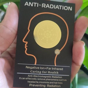 Puede incluir: Una tarjeta negra con el texto "ANTI-RADIATION" en letras blancas. La tarjeta presenta una pegatina dorada con un diseño circular y el texto "Negative Ion+Far Infrared Caring for Health Anti-Electromagnetic Radiation It can effectively remove phenomena such as headache, insomnia and hair loss Preventing Radiation".