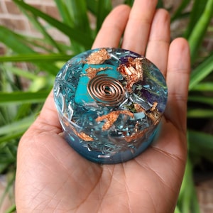 May include: A round, blue, resin orb with gold flakes, copper wire, and various crystals embedded inside. The orb is being held in a hand.