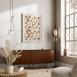 May include: A mid-century modern living room with a brown wooden cabinet, a white wall with a framed geometric print, a white fluffy armchair, and a hanging light fixture with two white glass globes.