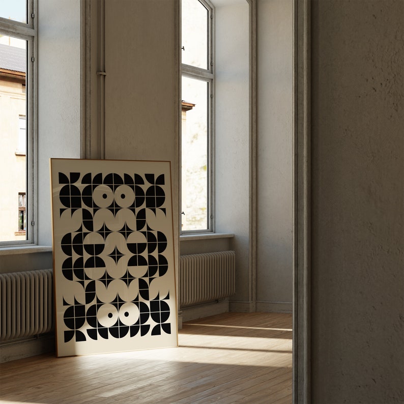 May include: A black and white geometric print in a gold frame hangs on a white wall in a room with large windows. The print features a repeating pattern of circles, semi-circles, and squares.