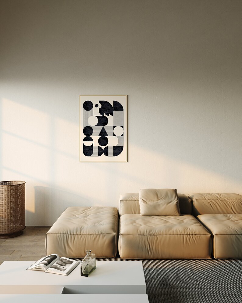 Puede incluir: Un sof&aacute; modular beige con una gran impresi&oacute;n geom&eacute;trica en blanco y negro enmarcada colgada en la pared detr&aacute;s de &eacute;l. El sof&aacute; est&aacute; en una sala de estar moderna con una mesa de caf&eacute; blanca y una cesta tejida.
