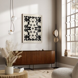 May include: A black and white geometric print in a wooden frame hangs on a white wall above a dark wood cabinet with a slatted front. The cabinet is on a light wood floor. There is a large window with white trim and a white wall behind the cabinet.