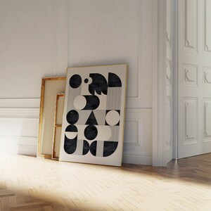 Puede incluir: Una impresi&oacute;n de arte abstracto geom&eacute;trico en blanco y negro con c&iacute;rculos, cuadrados y tri&aacute;ngulos. La impresi&oacute;n est&aacute; enmarcada en un marco dorado y se apoya contra una pared blanca.