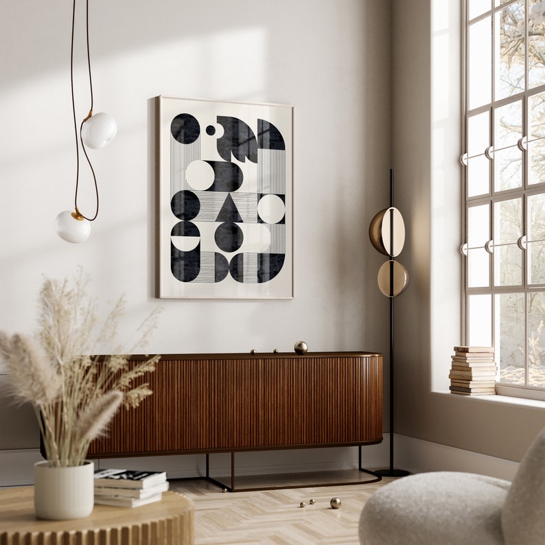 Puede incluir: Una impresi&oacute;n de arte abstracto geom&eacute;trico en blanco y negro en un marco blanco que cuelga de una pared blanca sobre un gabinete de madera oscura con un piso de madera clara.