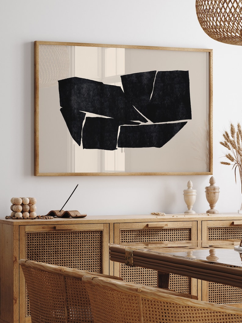 K&ouml;nnte beinhalten: Ein gerahmter abstrakter Kunstdruck mit einem geometrischen Design in Schwarzwei&szlig;. Der Druck h&auml;ngt an einer wei&szlig;en Wand &uuml;ber einem Holzschr&auml;nkchen mit geflochtenen Rattan-T&uuml;ren.