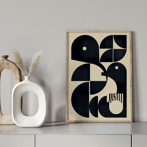 May include: A framed print featuring a geometric design in black and white. The design depicts a bird-like shape with a white dot in the centre of its head. The background is a light beige colour.
