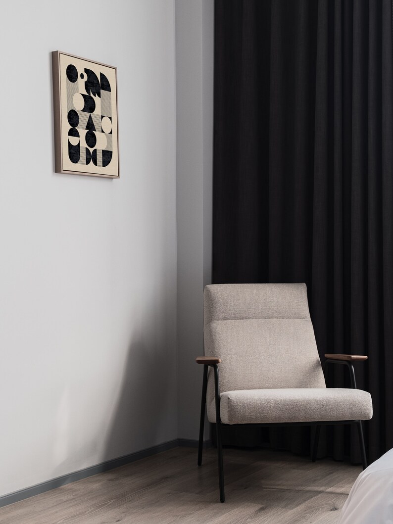 Puede incluir: Un sill&oacute;n beige con patas de metal negro y apoyabrazos de madera se encuentra en una habitaci&oacute;n con una pared blanca y cortinas negras. Un estampado enmarcado con un dise&ntilde;o geom&eacute;trico en blanco y negro cuelga de la pared.