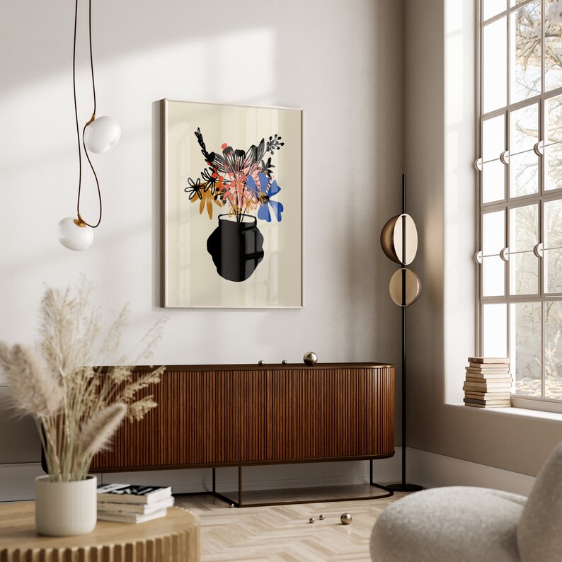Pu&ograve; includere: Una stampa incorniciata di un arrangiamento floreale stilizzato in un vaso nero. I fiori sono in tonalit&agrave; di blu, rosa, arancio e giallo. Lo sfondo &egrave; beige chiaro.