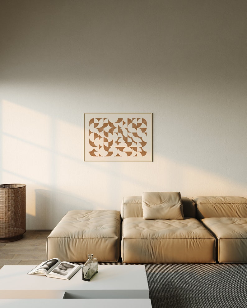 May include: A light beige sectional sofa with a brown geometric print framed artwork hanging on the wall behind it. The sofa is in a living room setting with a white coffee table and a woven basket in the background.