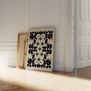 May include: A black and white geometric pattern print on a canvas in a gold frame. The print is hanging on a white wall.