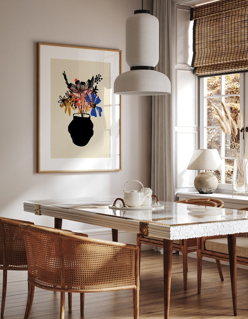 Pu&ograve; includere: Un tavolo da pranzo bianco con un piano a motivi bianchi e dorati, quattro sedie con sedute in vimini intrecciato e una lampada a sospensione in ceramica bianca sopra il tavolo. Una stampa incorniciata di un vaso di fiori &egrave; appesa al muro dietro il tavolo.