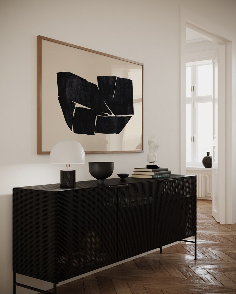 K&ouml;nnte beinhalten: Ein schwarzer Metallschrank mit einer Drahtgitterfront und zwei T&uuml;ren. Der Schrank steht auf einem Holzboden und hat eine Lampe, eine Sch&uuml;ssel und B&uuml;cher darauf. An der Wand hinter dem Schrank h&auml;ngt ein gerahmtes abstraktes Kunstbild.