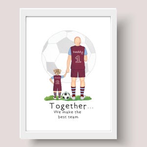 May include: A framed print featuring a father and child in soccer uniforms, standing on grass in front of a soccer ball. The father's jersey has the number 1 and the word "Daddy". The child's jersey has the number 2. Text at the bottom reads "Together... We make the best team."